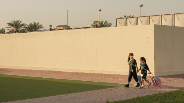 Sisters walking hand-in-hand while rolling backpacks outside The WellSpring Private School about to go to class